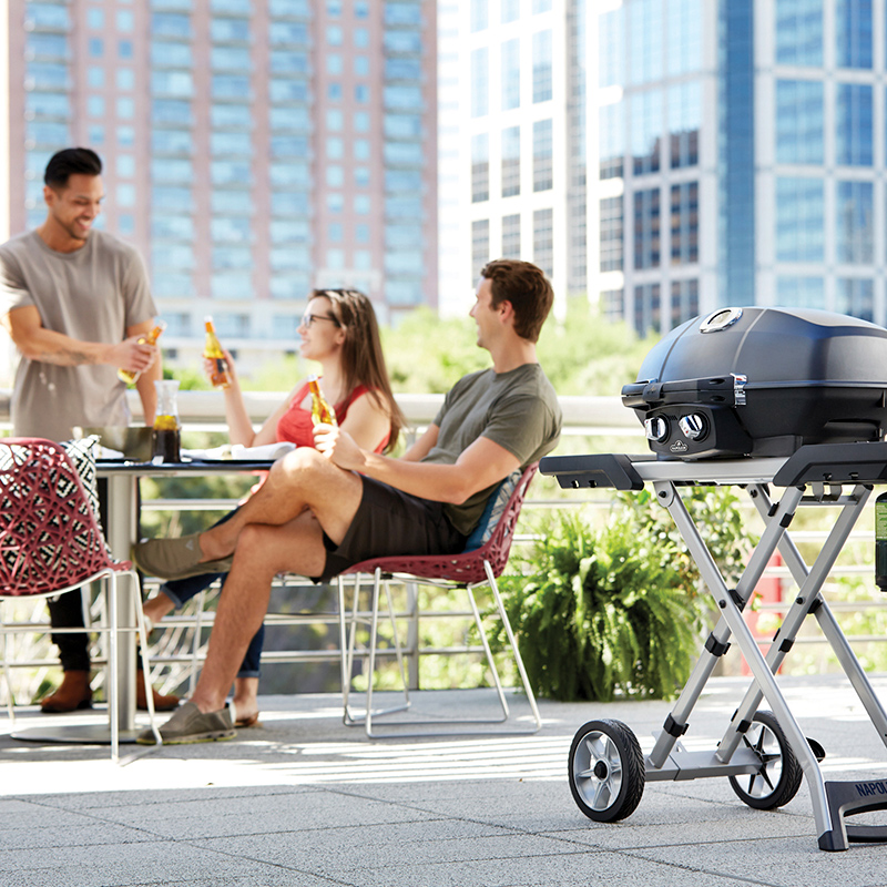 Kolme ystävää nauttii juomia kaupunkikatolla, taustalla pilvenpiirtäjiä ja musta kaasugrilli.