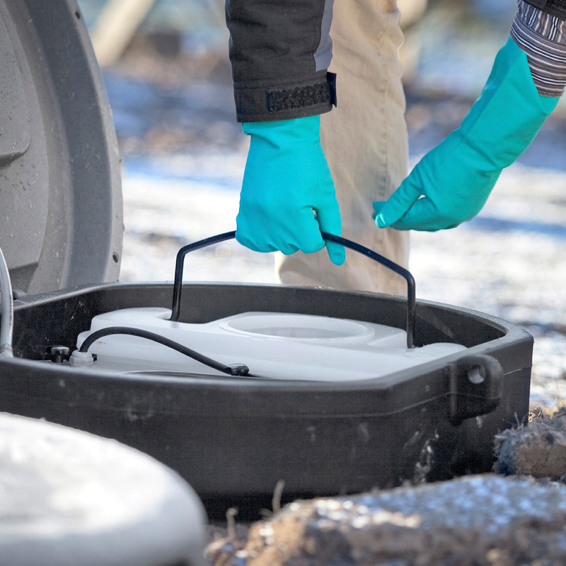 Turkoosit suojakäsineet nostavat valkoista säiliötä mustasta laatikosta lumisella pihalla.