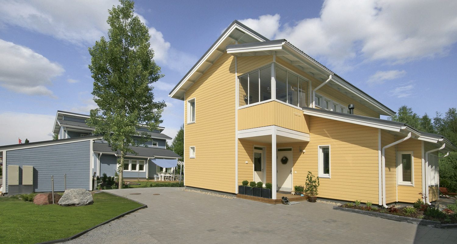 Keltainen kaksikerroksinen puutalo valkoisin yksityiskohdin, lasiparveke, edessä sininen talo.