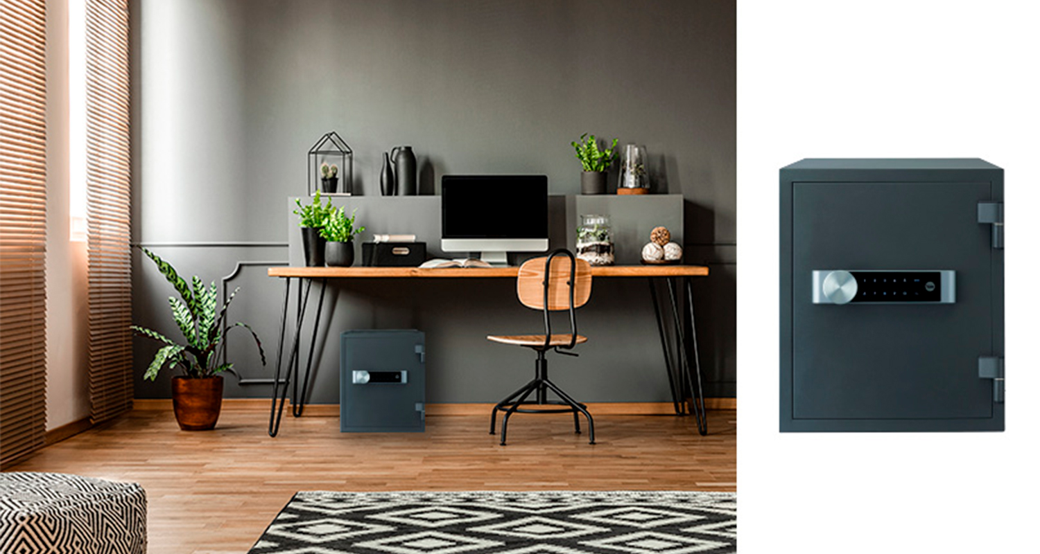 Tyylikäs kotitoimisto: puupöytä, näyttö, vihreät kasvit, tuoli ja musta-harmaa seifi