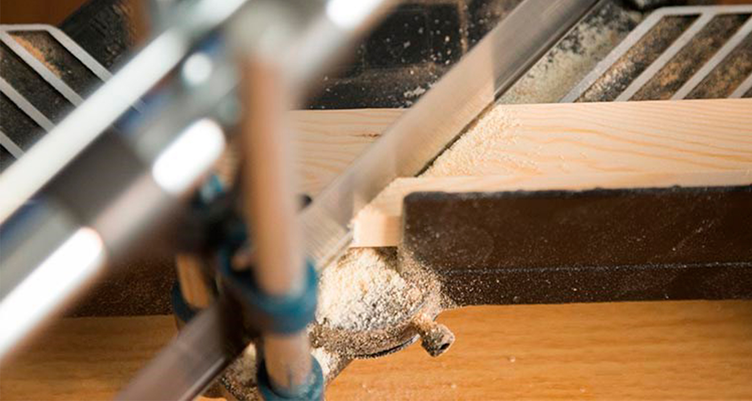Hopeinen pöytäsaha leikkaa vaaleaa lautaa, sahajauhoa leviää pöydälle.