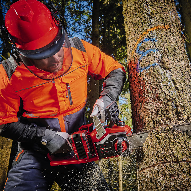 Oranssipukuinen sahaaja sahaa punaista moottorisahaa puunrunkoa jossa sininen ja oranssi merkki