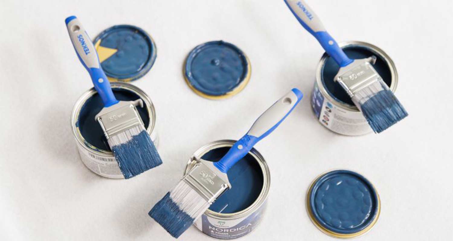 Avoimet siniset maalipurkit ja siniset pensselit valkoisella alustalla