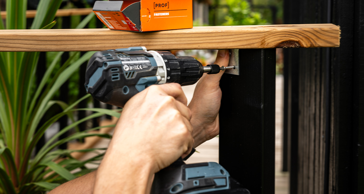 Tee itse terassikaide: Mies kiinnittää yläkaidepuuta.