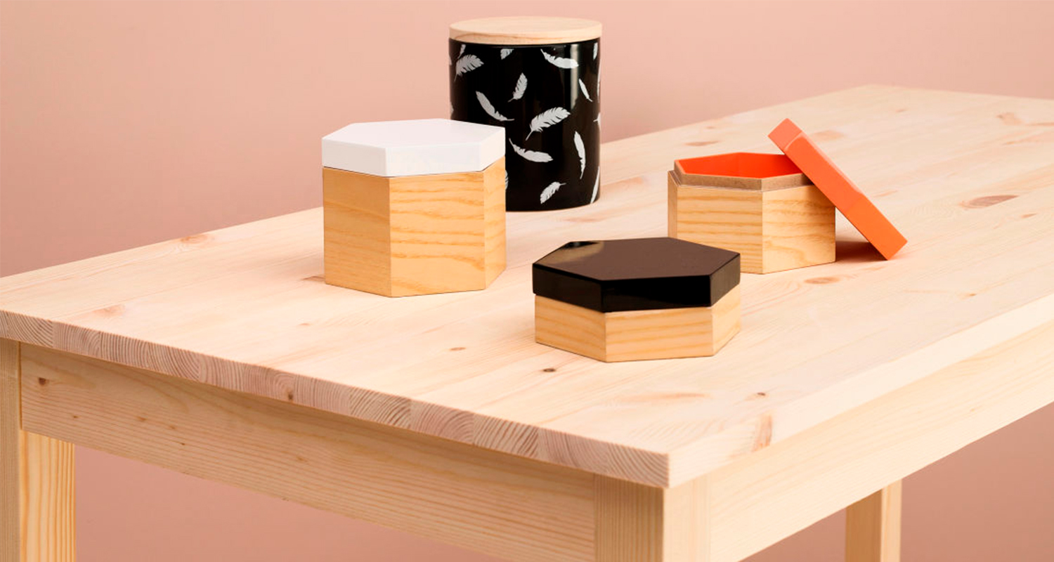 Vaalean puun pöydällä neljä puurasiaa eri kansivärein: valkoinen, musta, höyhenkuvio ja oranssi