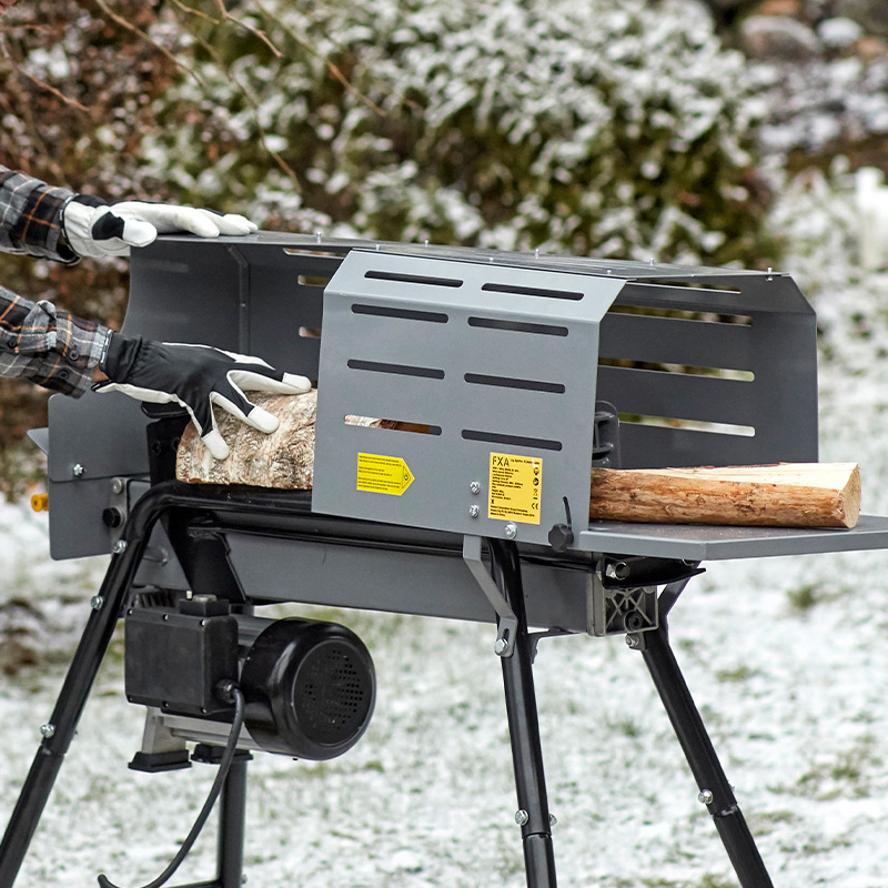 Harmaa musta polttopuunhalkomakone, käsineet syöttävät halkoa lumisessa pihassa