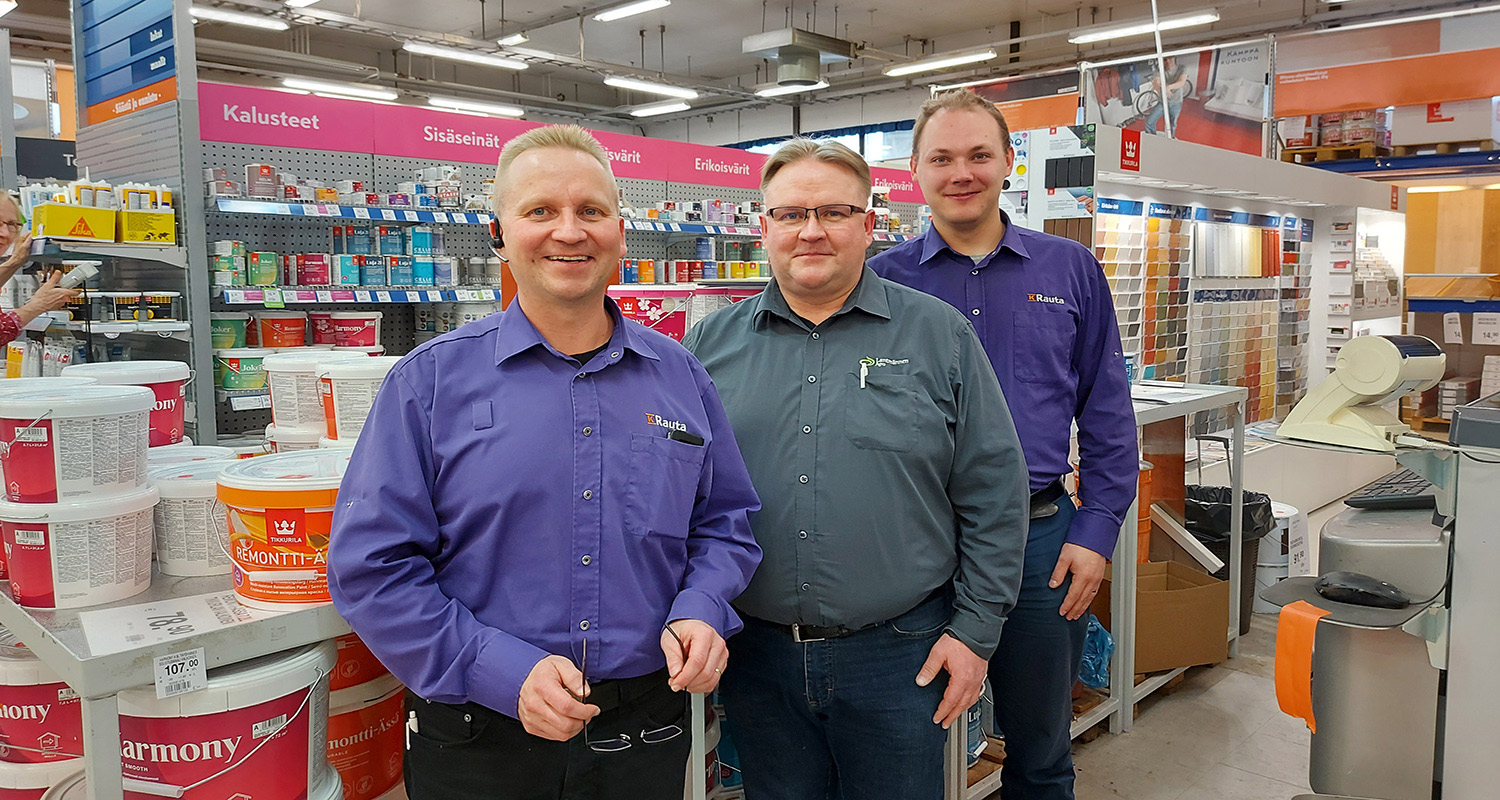 Kolme Rauta-myymälän työntekijää violeteissa ja harmaissa paidoissa maali- ja sisustusosastolla.