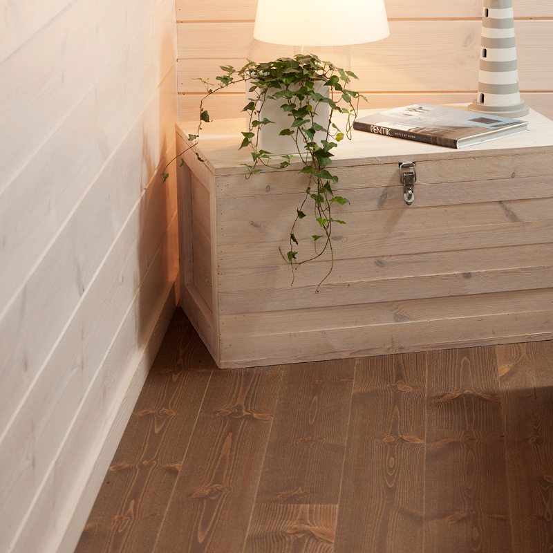 Vaalea puulaatikko nurkassa, valkoinen lamppu ja roikkuva viherkasvi tummaa puulattiaa vasten