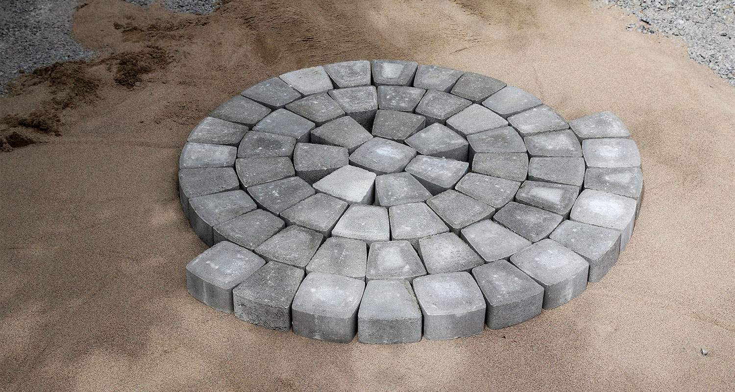 Harmaat betonikivet aseteltu pyörökuvioon hiekkapohjalle.