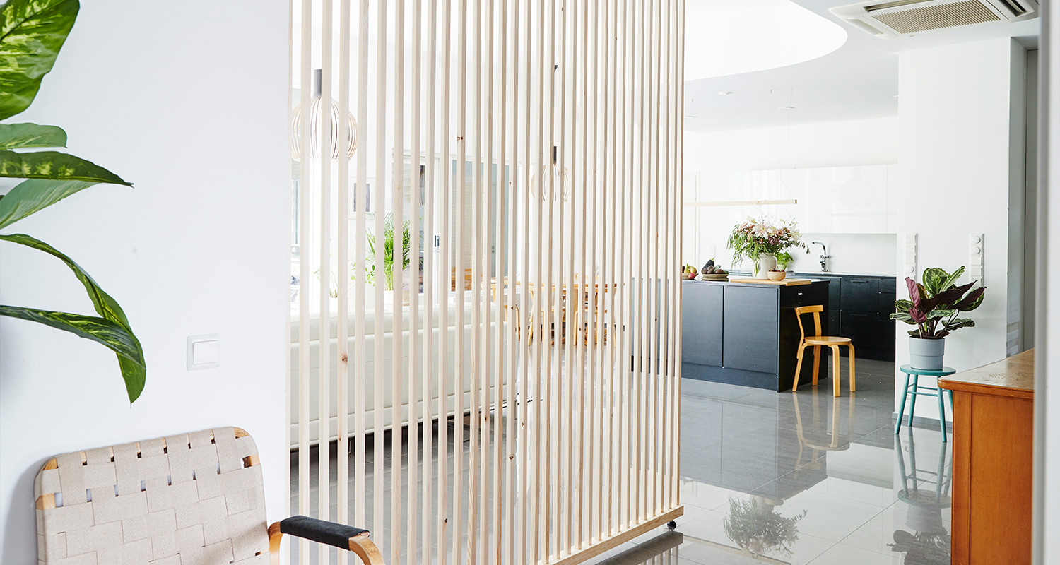 Moderni valoisa avokeittiö ja olohuone, puinen rimoitusväliseinä, musta saareke, viherkasveja.