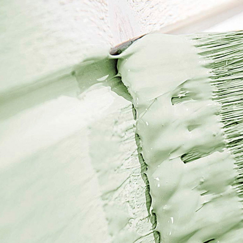 Kuvassa vaalean vihreää pohjustemaalia. Maalia levitetään seinään maalisiveltimellä.