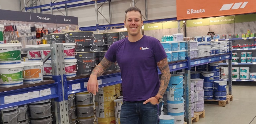 Mies violetti T-paita K-Raudan hyllyjen edessä maalipurkkien keskellä