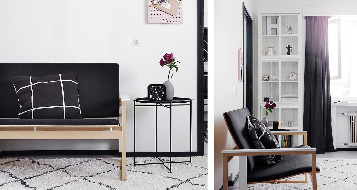 Vaalea minimalistinen olohuone, musta-puinen nojatuoli, pyöreä sivupöytä kello ja pinkki maljakko.
