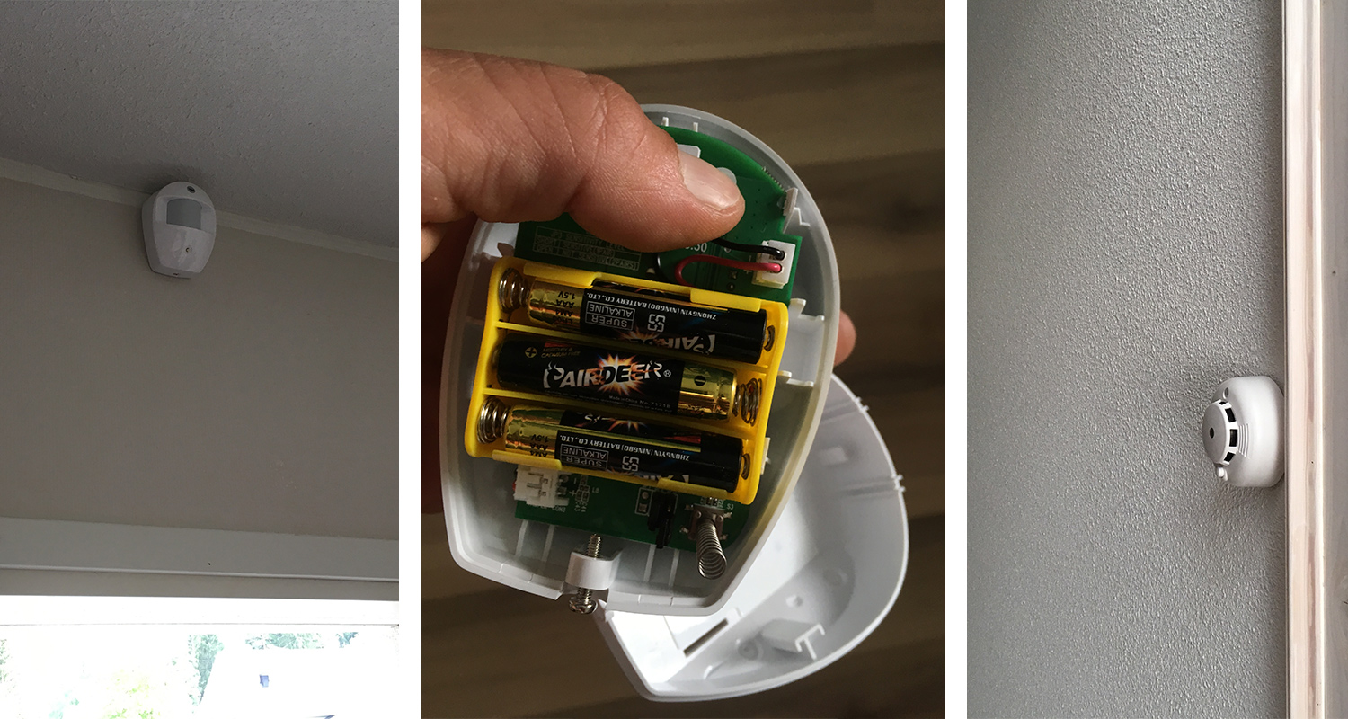 Valkoinen liiketunnistin ikkunan yllä, auki oleva paristokotelo ja savuilmaisin harmaalla seinällä.