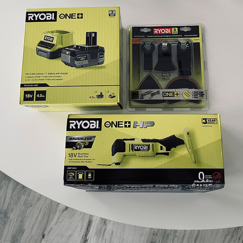 Pöydällä valmiina kokeiluun Ryobin akkumonitoimikone akkupaketin ja teräsarjan kera.