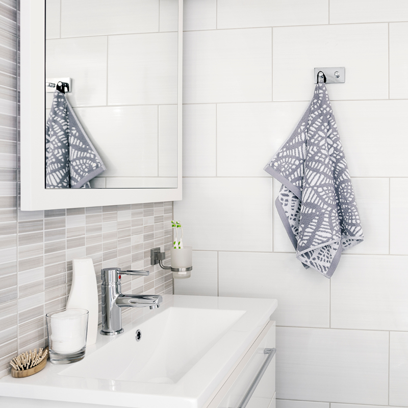 Valkoisessa kylpyhuoneessa allas, kromihana, peili ja harmaa kuvioitu pyyhe