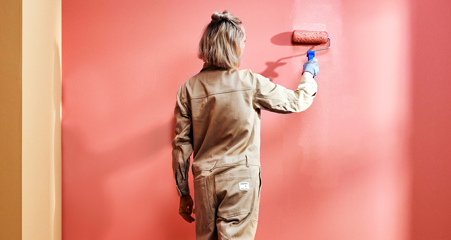 Nainen maalaa seinää. Seinät maalattu kahdella eri värillä: Tikkurilan sisämaalisävyt K419 ja J404.