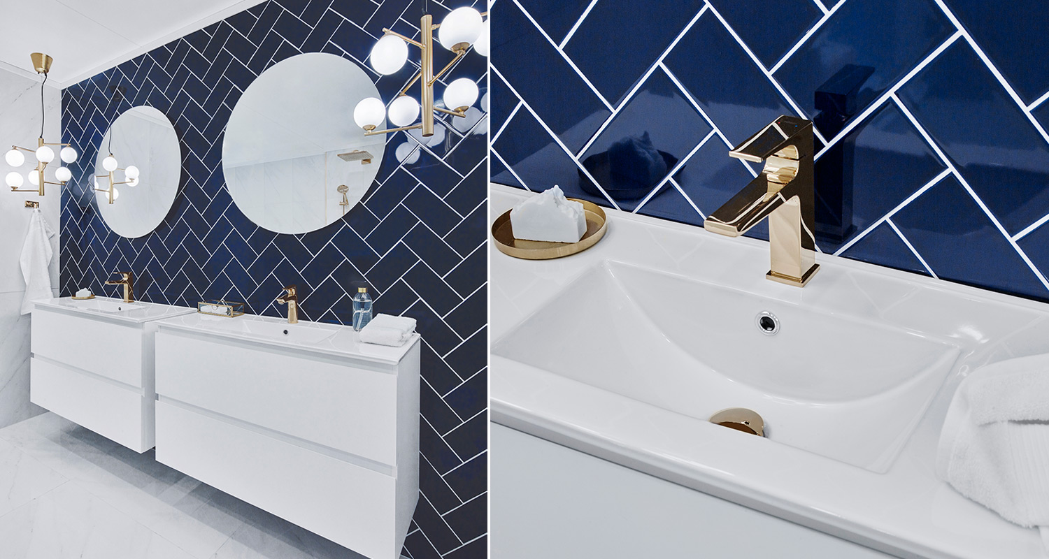 Moderni kylpyhuone: valkoiset allaskaapit, tummansininen kalanruotaseinä, kultaiset hanat ja peilit