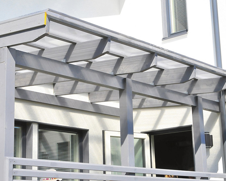 Valkoisen talon edustalla harmaa pergola läpinäkyvällä katoksella ja avoin terassiovi.