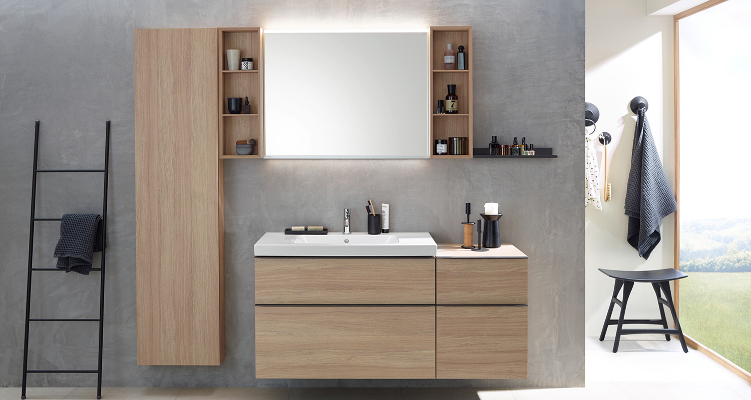 Vaalea puuallas ja hyllypeili betoniseinällä, musta pyyheteline ja metsämaisema ikkunasta