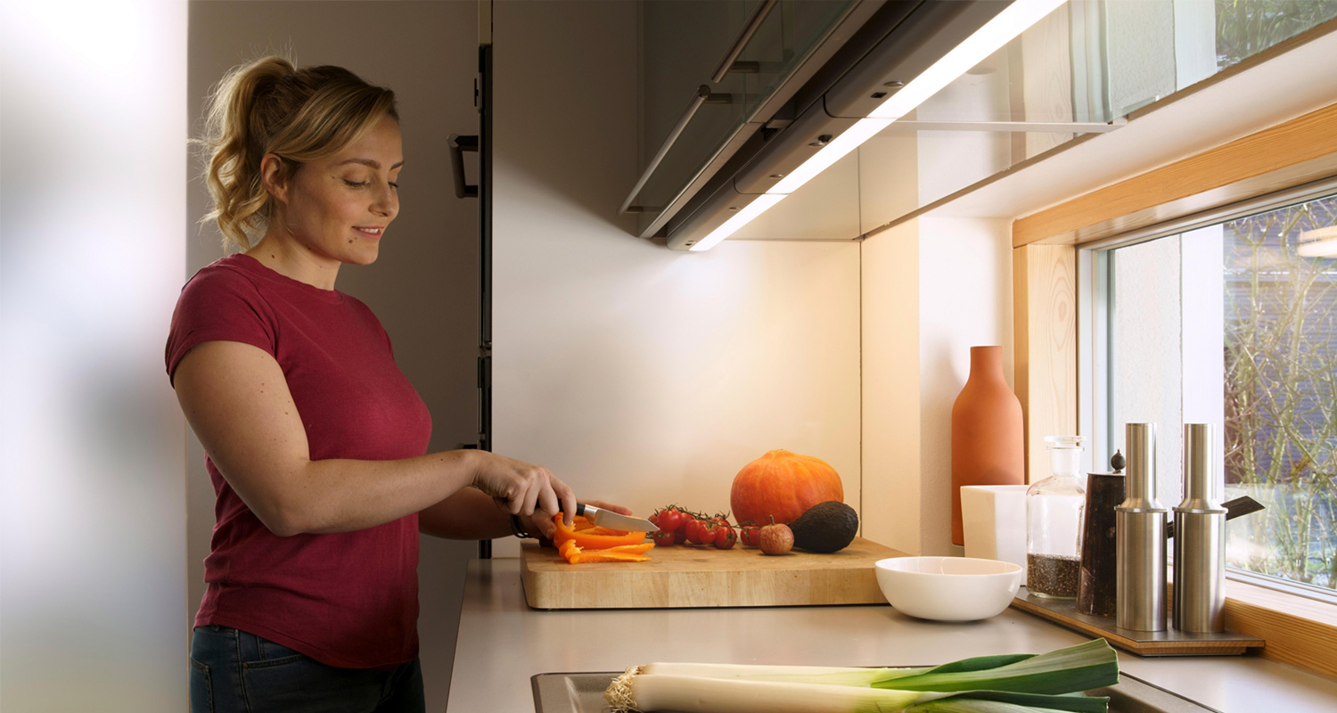 Modernissa keittiössä henkilö pilkkoo oranssia paprikaa puuleikkuulaudalla ikkunan ääressä.