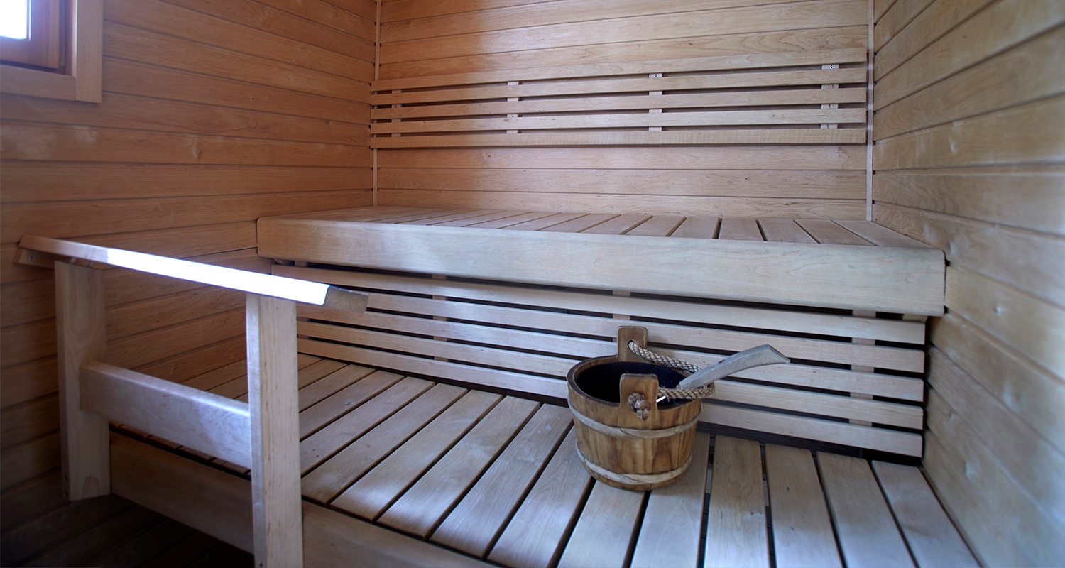Vaalea puusauna, kaksitasoiset puulauteet, vesisanko kauhalla ikkunan valossa