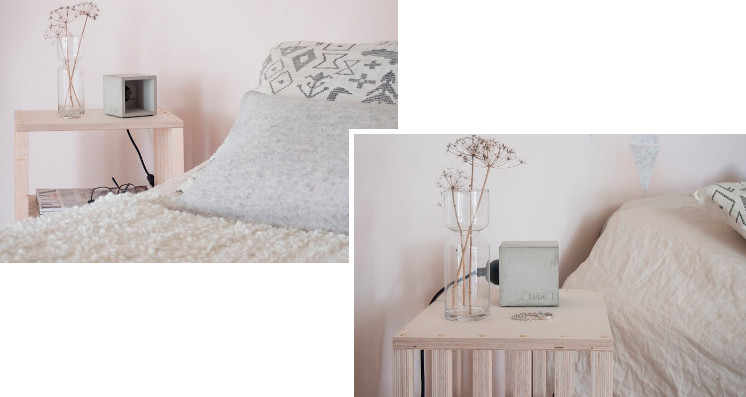 Vaaleapuisella yöpöydällä maljakko kuivilla kukilla ja betonikaiutin vaaleanpunaisessa huoneessa