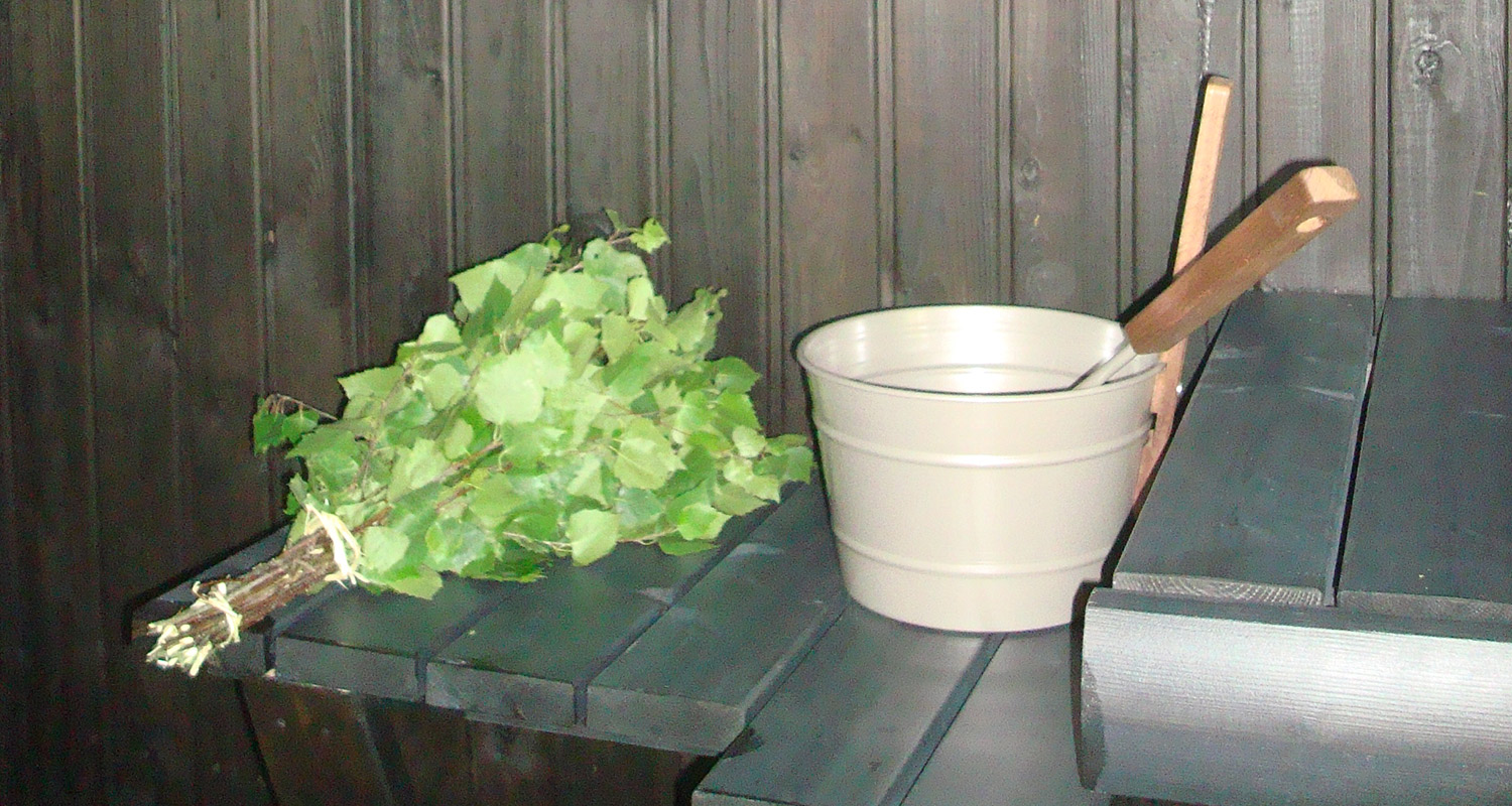 Saunan tumma laude, vihdanoksakimppu ja vaalea vesikauha puisella kauhalla