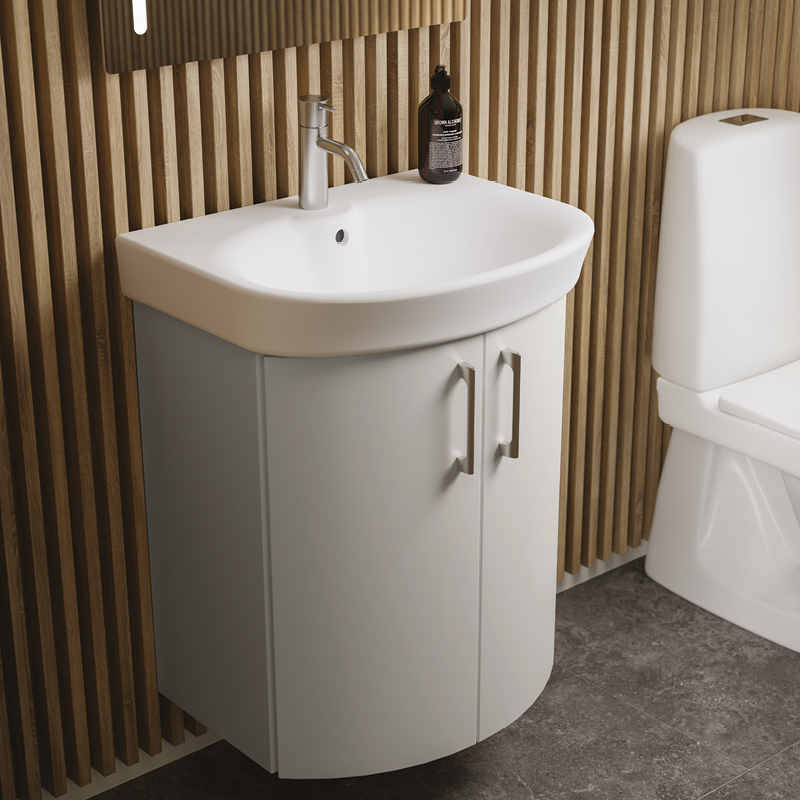 Valkoinen pyöristetty allaskaappi puupaneloitu seinä, vieressä WC ja musta saippuapullo