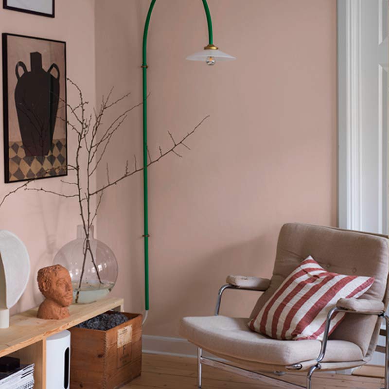 Kuvassa vaalean roosa yksivärinen tapetti, vaalea puulattia ja vihreä lattiavalaisin.