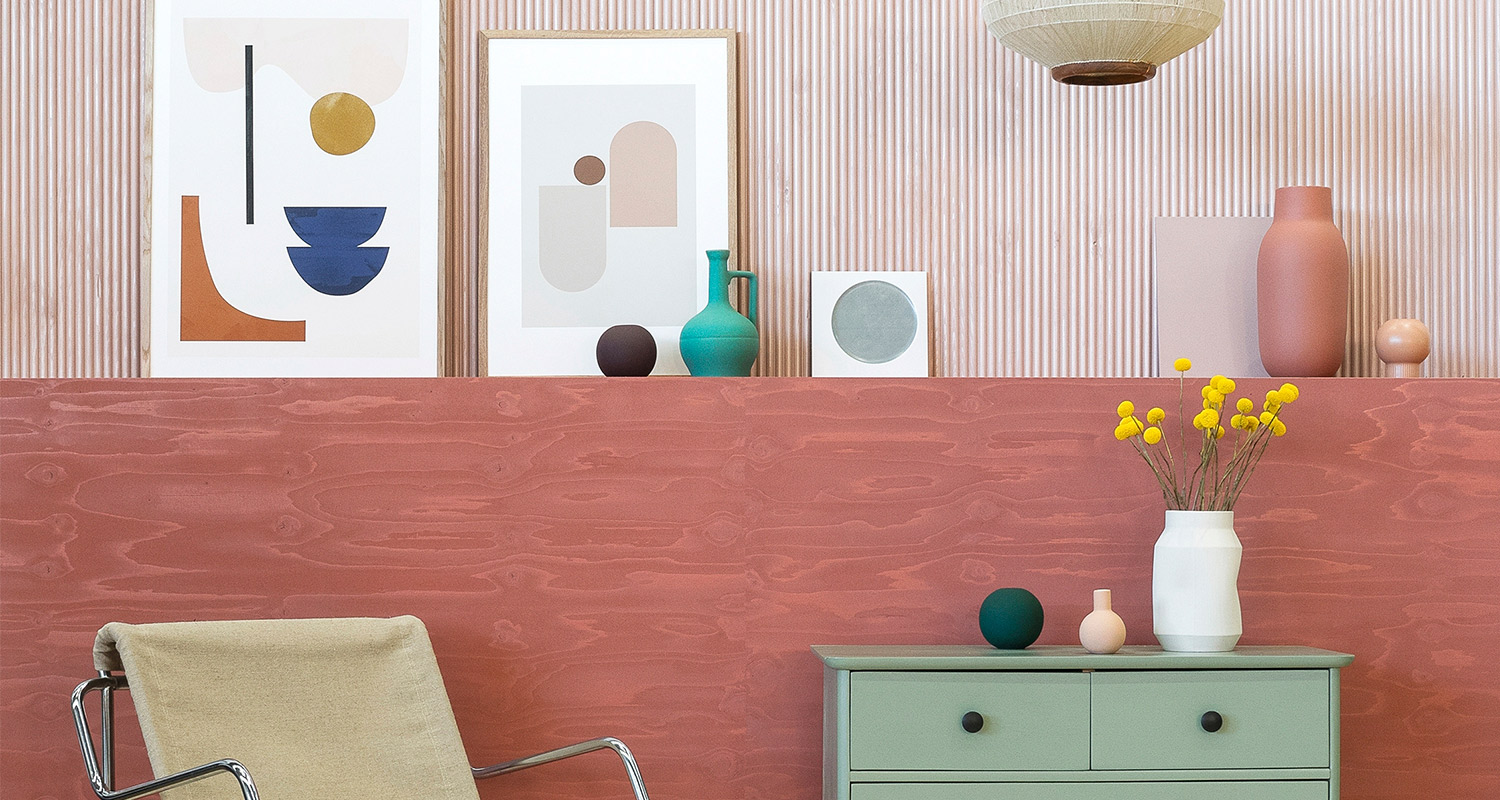 Vaaleanpunainen seinä, abstraktit taulut, mintuvihreä lipasto ja maljakko keltaisilla kukilla
