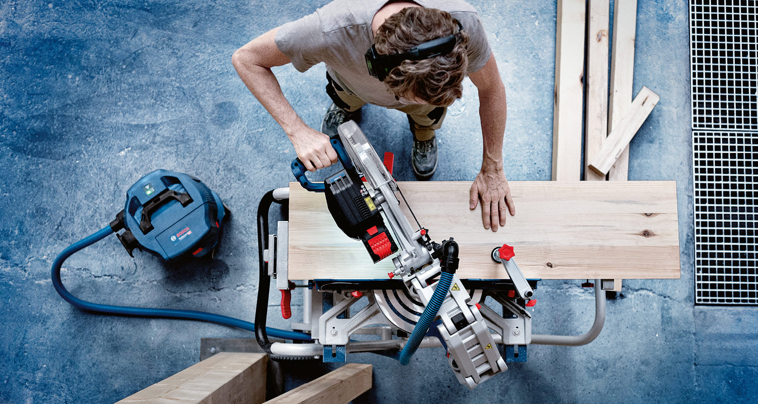 Työpajassa ylhäältä kuvattu mies sahaamassa vaaleaa puulankkua sinisellä imurilla.