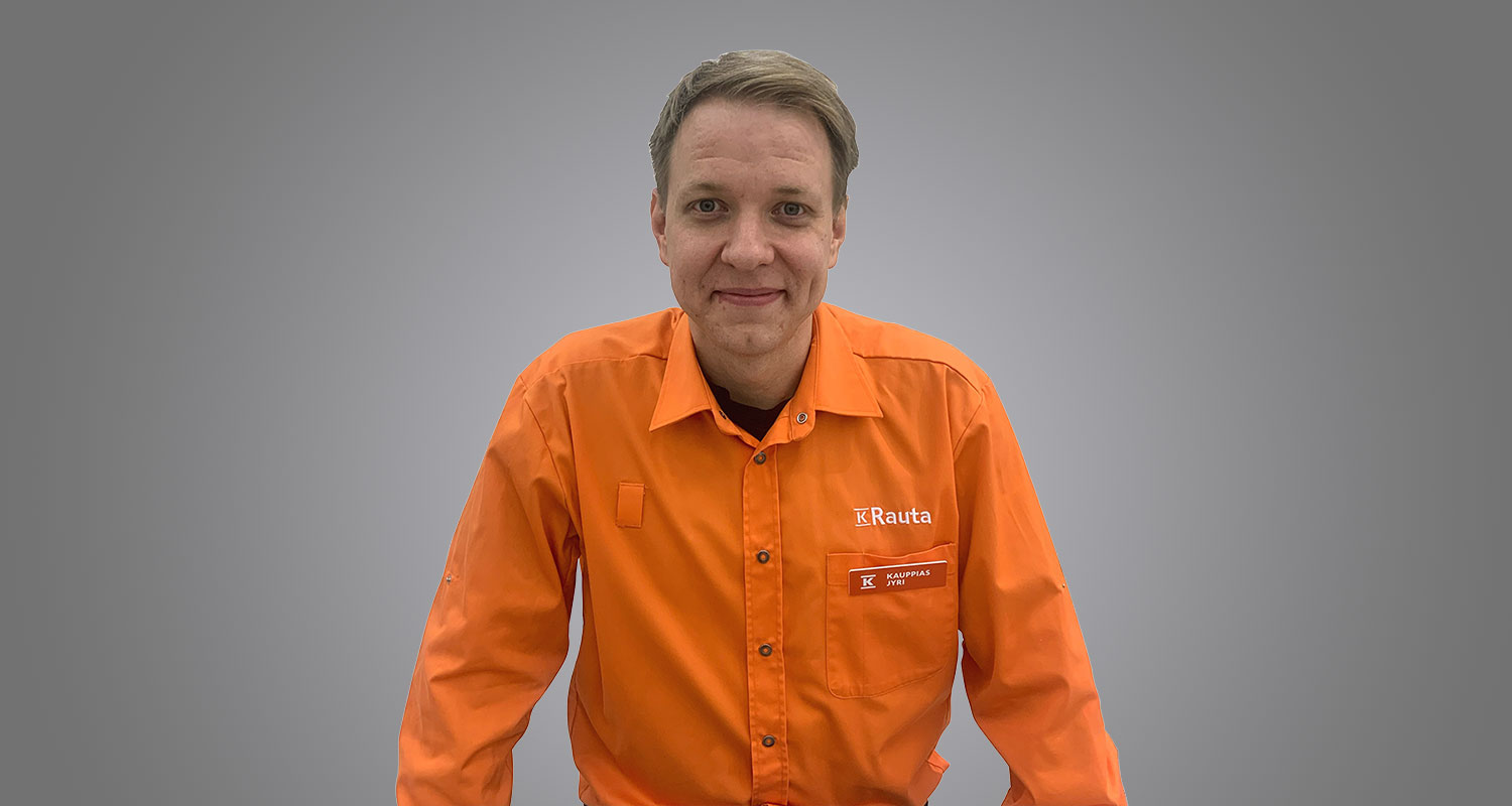 Oranssi K-Rauta-paita logolla ja nimikyltillä, harmaan seinän edessä.