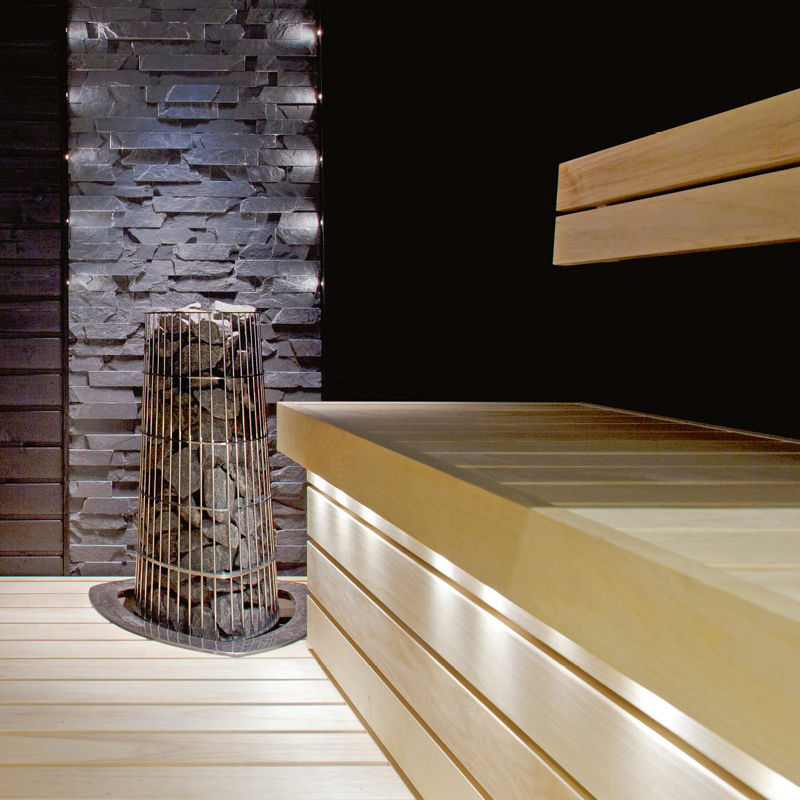 Saunan vaaleat puulauteet ja lattia, musta kiviseinä ja metallikehikko täynnä kiuaskiviä.