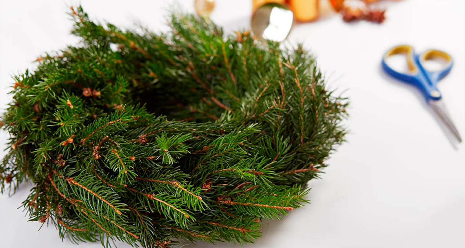 Joulukranssi valmistuu havujen sitomisella. Pöydällä joulukranssi sekä sakset.