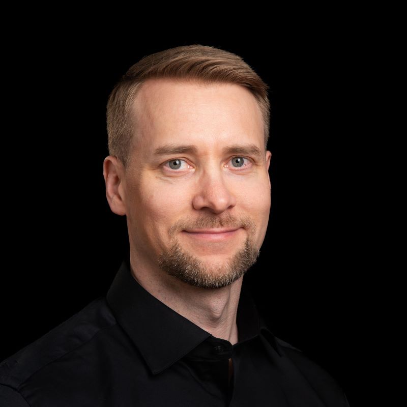 Vaaleahiuksinen henkilö mustassa paidassa tumman taustan edessä.