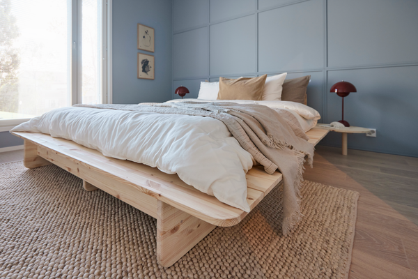 Matala puinen sänky valko-beigeillä peitoilla, sininen paneeliseinä ja punaiset yöpöytälamput