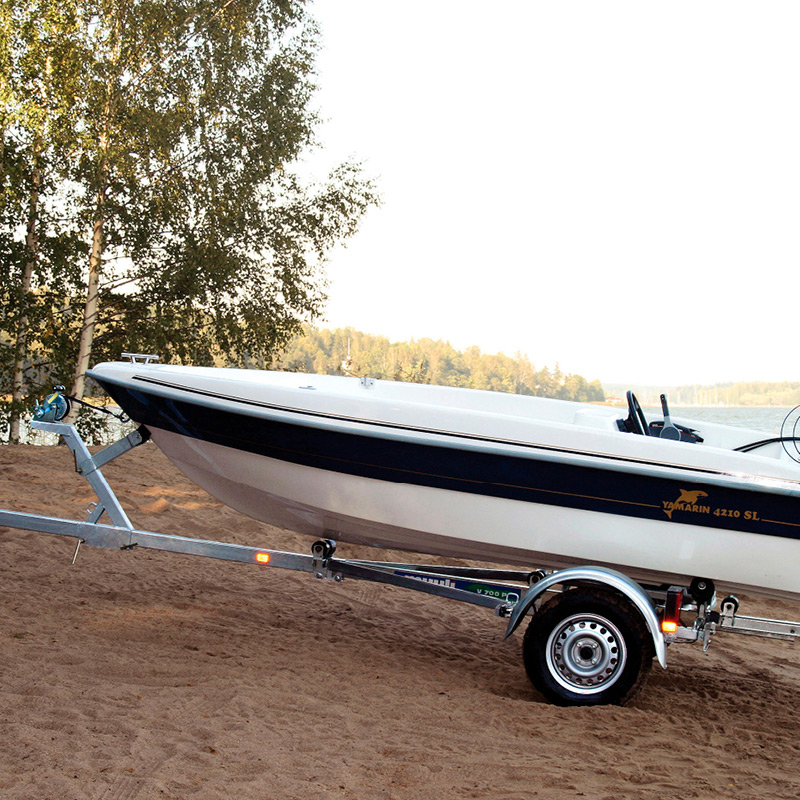 Valkoinen-tummansininen moottorivene kärryssä järven hiekkarannalla koivun juurella