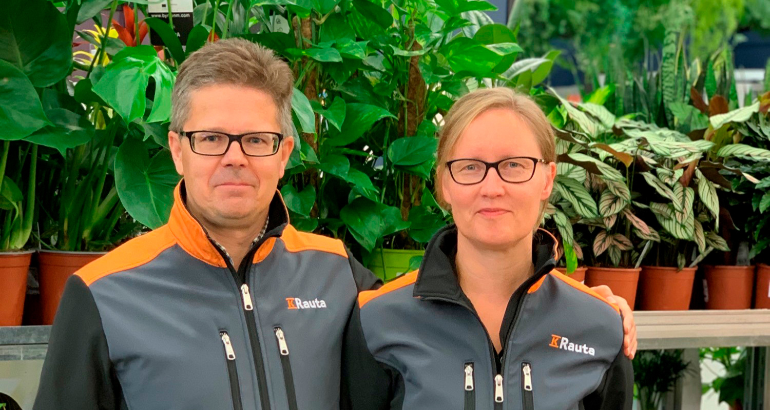 Kaksi Rauta-työntekijää harmaissa-oransseissa takeissa viherkasvien keskellä.