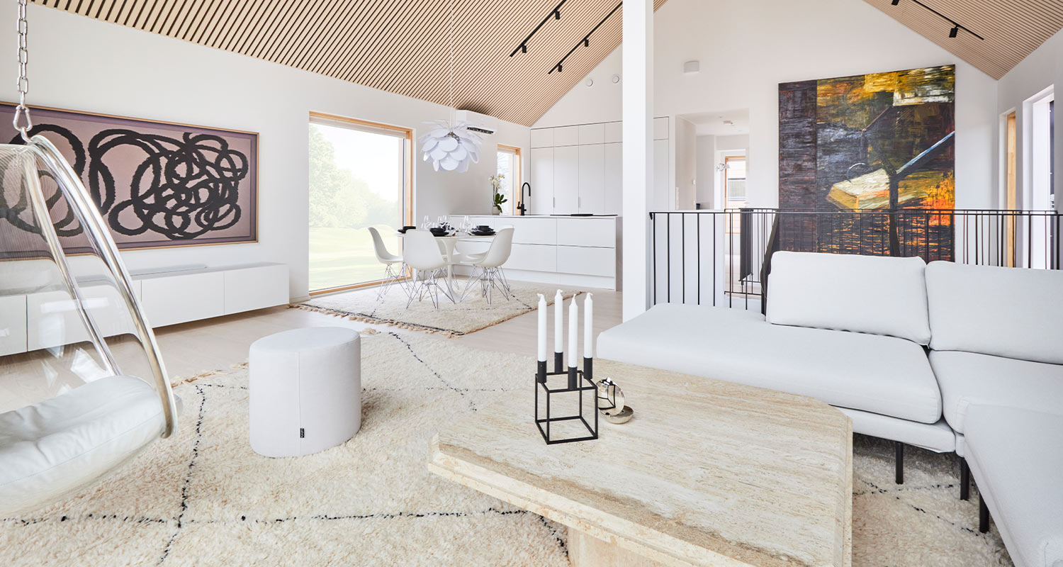 Avoin olohuone-keittiö: valkoiset kalusteet, puukuvioitu katto, abstraktit seinämaalaukset.