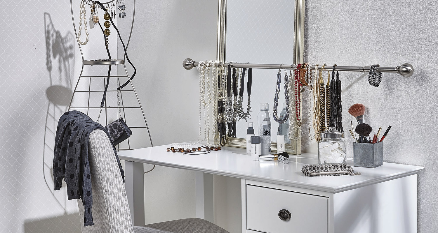 Valkoinen meikkipöytä peileineen, hopeinen korutanko roikkuvine kaulakoruineen ja siveltimineen