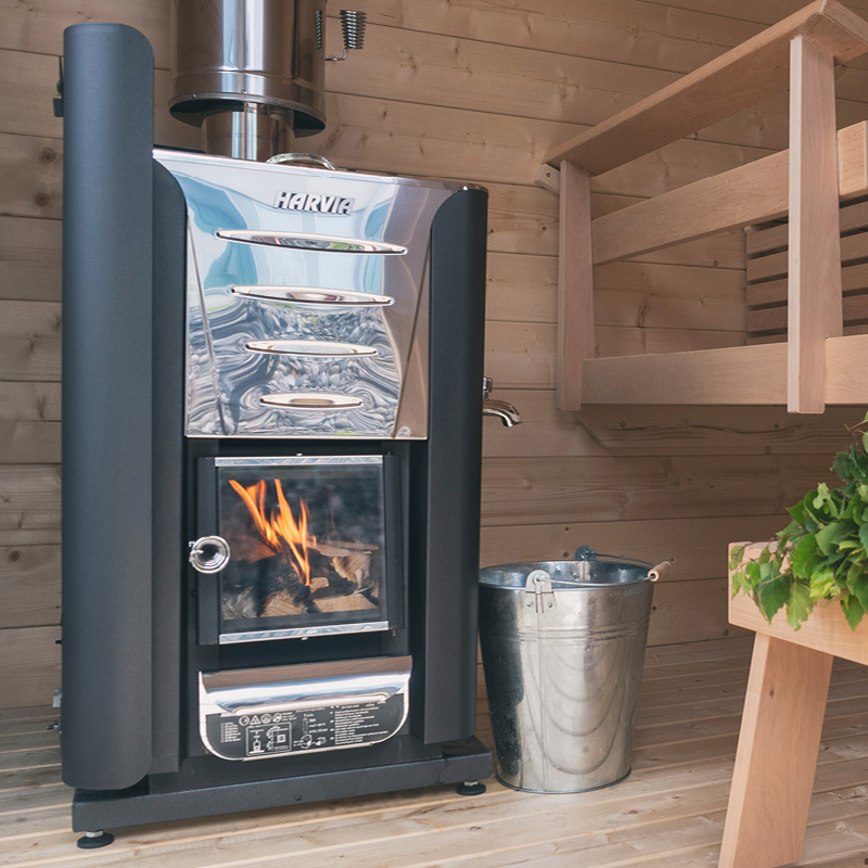 Harvian musta-harmaa saunauuni liekehtivällä tulipesällä, vieressä sinkkiämpäri ja puupenkki