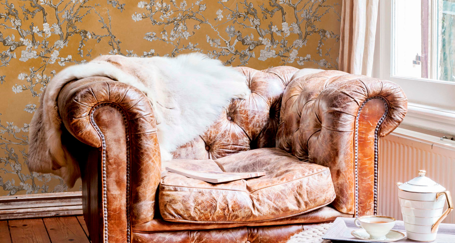 Ruskea nahkainen nojatuoli valkoisella lampaankarvapeitteellä kirja ja teeastiasto ikkunan ääressä