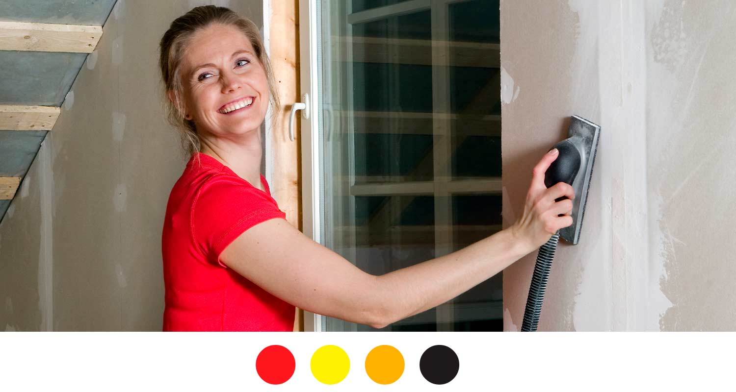 Punapaitainen hioo ikkunan vieressä kipsiseinää letkuhiomakoneella