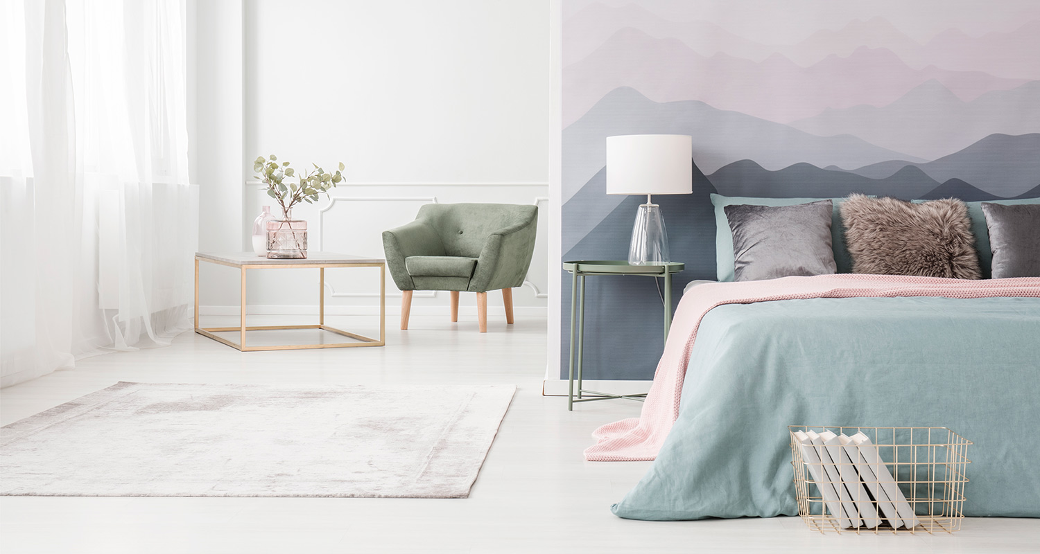 Valoisa huone: sininen sänky pinkillä viltillä, vihreä nojatuoli ja pastellivuoriseinä
