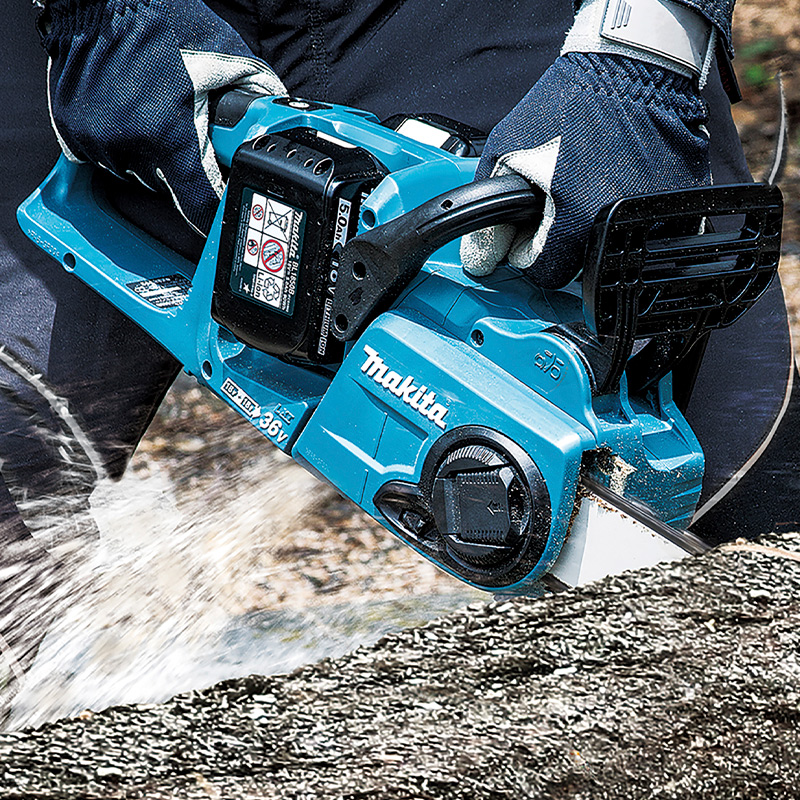 Käsineet pitävät sinistä Makita-akkuista ketjusahaa sahaten tukin, purua roiskuu.