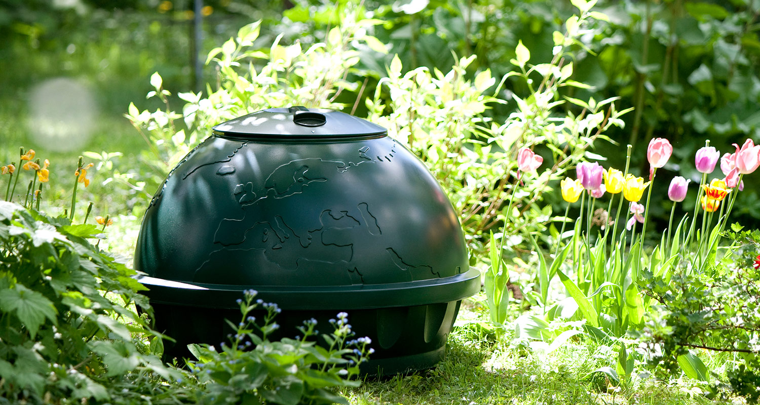 Pyöreä, tummanvihreä kompostori kesäisessä puutarhassa, ympärillä värikkäät tulppaanit