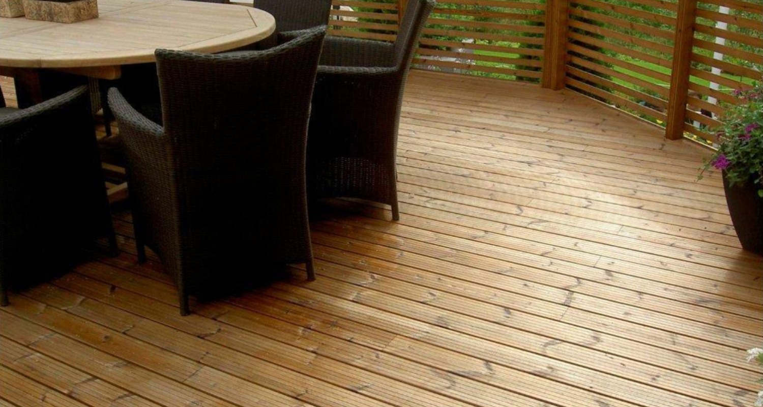 Vaalea puulattia ruskeine punottuine tuoleineen, pyöreä pöytä ja kukkiva ruukku