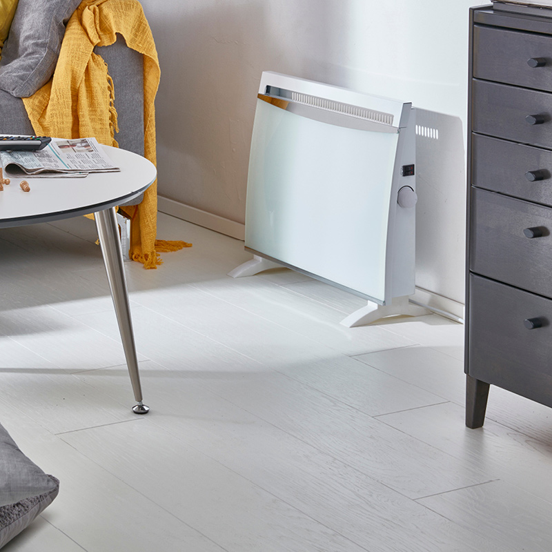 Harmaa sohva jossa keltainen viltti, valkoinen pyöreä pöytä ja valkoinen lattialämmitin.