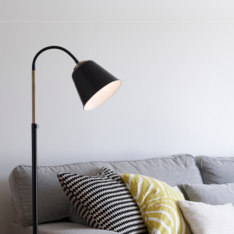 Musta lattiavalaisin valaisee harmaata sohvaa, jossa mustavalkoinen ja keltainen koristetyyny.